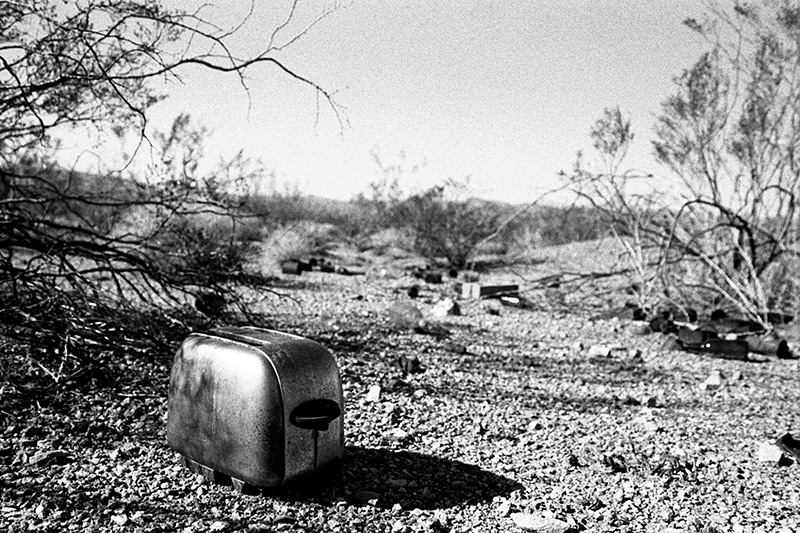 toaster on floor of desert with bottle scattered behind