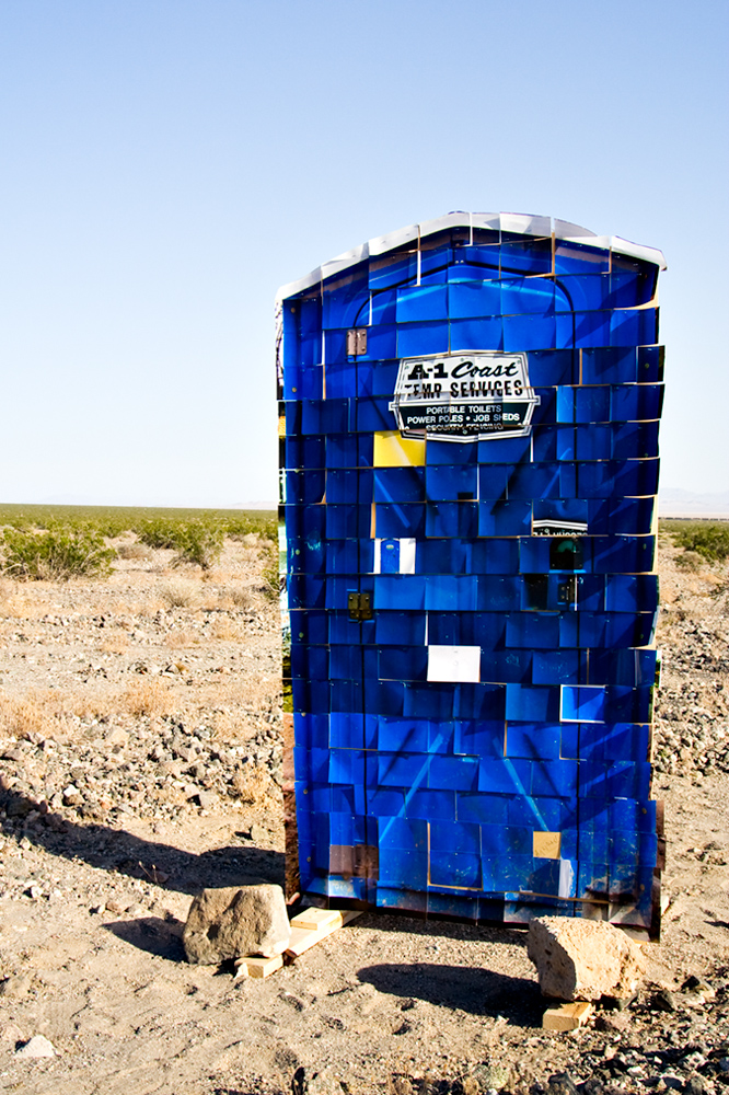 150 4x6 photos stapled to plywood in the shape of a porta potty